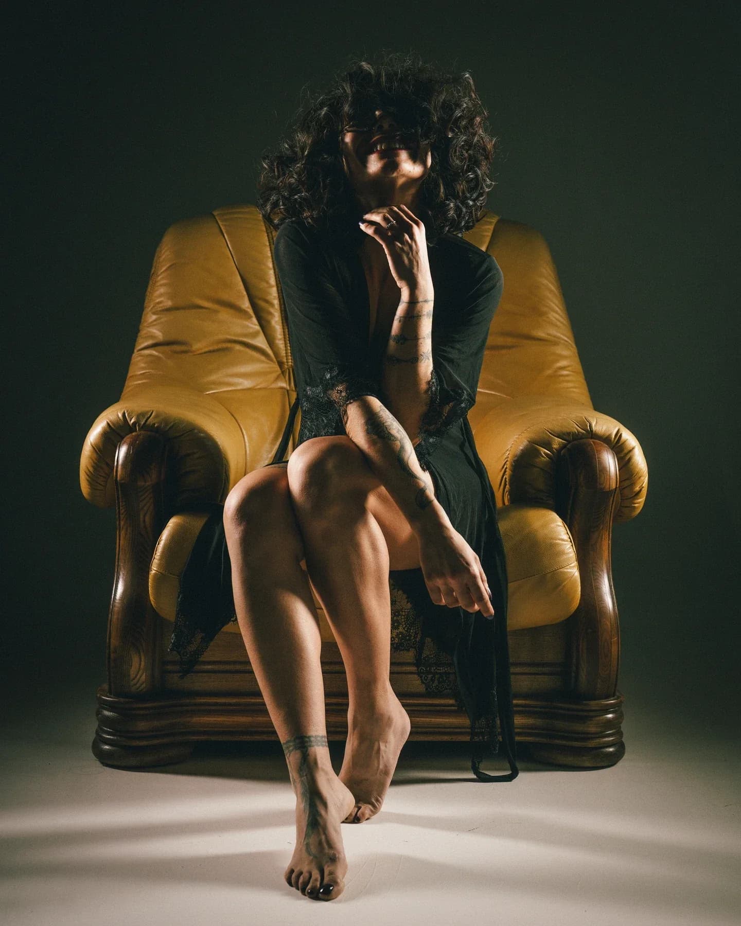 Femme assise dans un fauteuil doré, fond sombre et lumière rasante